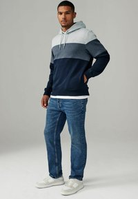 Hoodie met een grijs en marineblauwe kleurblokontwerp, van een katoenmix, met een voork pocket, gecombineerd met blauwe jeans en witte sneakers.
