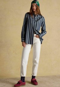 Tumestriipidega nööpitud särk valgete triipudega, koos valgete pükstega ja burgundi punaste kingadega. Isikul on peas roheline lilleline sall.