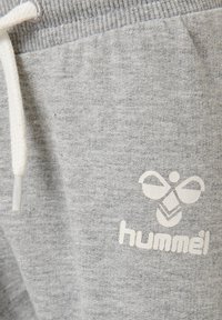 Grå bomullsoveraller med en vit logotyp och text, med dragsko i midjan och strukturerad tyg för komfort.