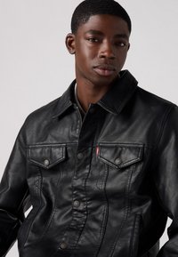 Veste en cuir noir avec un col, un front à boutons et deux poches poitrine. Texture lisse et couture présente partout.
