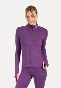 Purple athletic jacket with a high collar, full zipper, and side pockets; smooth texture with fitted sleeves. Paired with matching leggings.