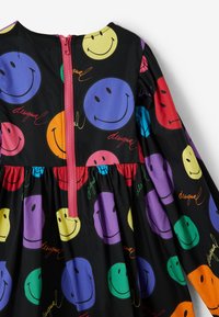 Czarna sukienka z wielokolorowymi wzorami uśmiechniętych buziek w kolorach fioletowym, zielonym, czerwonym, żółtym i niebieskim. Posiada ukryty różowy zamek błyskawiczny i marszczony dół.