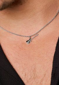 Collana d'argento con un piccolo ciondolo a forma di chitarra, dettagliata con corde e forma del corpo, posizionata su pelle.