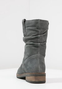 Bottine en daim gris au design décontracté, à talon plat et avec des détails de couture. Présente un haut replié et un accent en bois au niveau du talon.