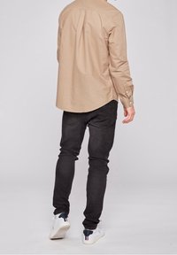 Lichtbeige overhemd met knopen en omslagen bij de mouwen, gecombineerd met zwarte slim-fit jeans en witte sneakers met marineblauwe en rode accenten.