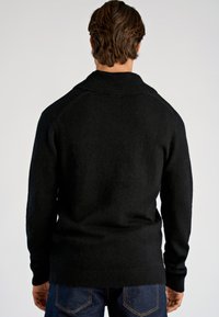 Schwarzer Strickpullover mit Schalkragen, gerippten Bündchen und Saum, aus strukturiertem Stoff mit legerer Passform. Trägt sich über dunklem Denim.