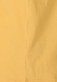 Gul bomullstyg med en mjuk textur, med en söm som löper vertikalt längs ena sidan. Minimalistisk design, utan synliga mönster eller detaljer.