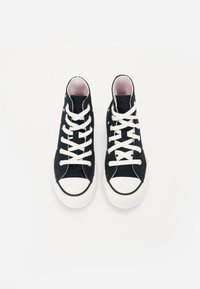 Pár černých vysokých tenisek s bílými šněrovacími tkaničkami a špičkami, zdobených malými barevnými hvězdnými vzory, viděný zvrchu na bílém pozadí.