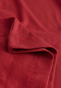 Ribbed red cotton textile with a smooth texture, showcasing folded edges and visible stitching details.