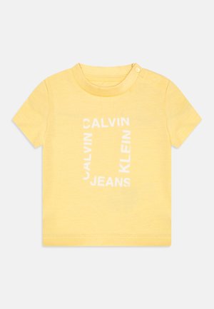 Yellow cotton T-shirt featuring short sleeves, a round neck, and a white graphic text design that reads "CALVIN KLEIN JEANS."