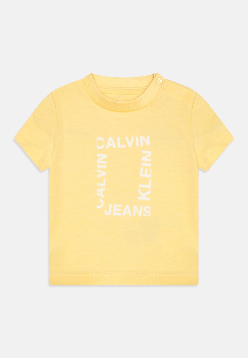 Žluté bavlněné tričko s krátkými rukávy, kulatým výstřihem a bílým grafickým textem, který zní "CALVIN KLEIN JEANS."