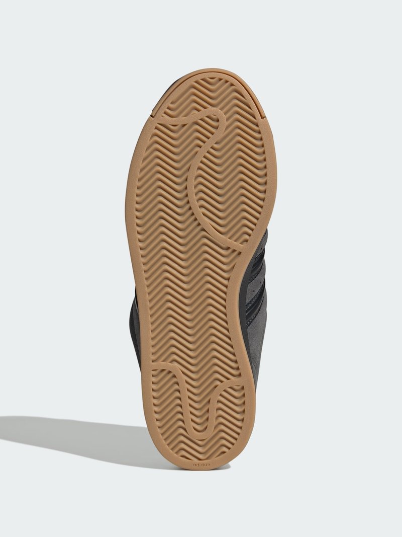 Svart sneakersula med vågmönster i gummi och beige accenter; har en strukturerad yta och sidomärke för grepp.