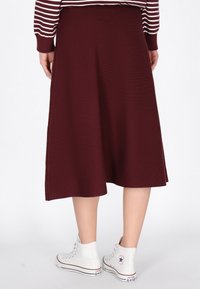 Burgundy polvisullinen hame, jossa on teksturoitu kangas, laajennettu leikkaus ja yhdistetty valkoisiin korkean varren tennareihin.