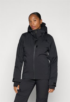 Chaqueta aislante negra con cremallera frontal, capucha ajustable y puños de Velcro. Presenta acentos de logo y un diseño elegante y moderno.