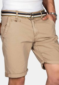 Beige cotton shorts with rolled hems, featuring side pockets and a multicolored striped fabric belt secured with a metal buckle.