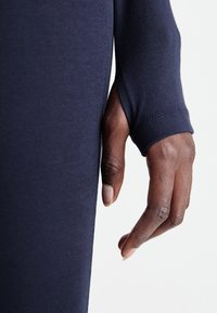Tumesin pikkvarrukaga riietus, millel on sobiv ja sooneline tekstuur. Suurem lähenemine käele näitab varruka üksikasju ja sujuvat kangast.