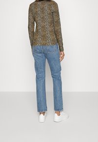 Långärmad topp i leopardmönster kombinerad med ljusblå denimjeans. Vita sneakers syns vid fötterna. Enkel design med en figurnära siluett.