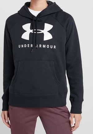Zwarte Under Armour hoodie met groot wit logo en tekst, gedragen door een persoon in kastanjebruine broek met ontspannen handen langs de zij.