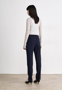 Pantaloni tailored blu navy con una silhouette a gamba dritta, dotati di una cintura elegante e tasche posteriori, abbinati a un top leggero a coste.