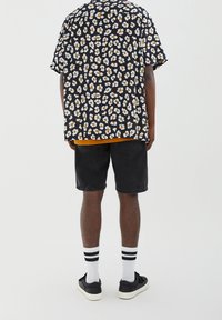 Black short-sleeved shirt with white and orange floral pattern, paired with dark shorts, white socks with black stripes, and black sneakers.