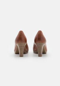 Paire de chaussures à talons hauts en cuir marron vues de dos, avec des talons en bois empilés, sur un fond blanc.