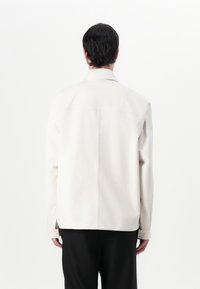 Lichtbeige overshirt met een klassieke kraag, rechte snit en knopen op de mouwen. Zachte textuur, minimalistisch ontwerp en geen patronen.