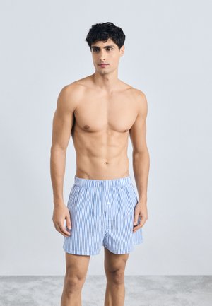 Boxer blu e bianchi a righe realizzati in tessuto leggero, con una vita elastica e una chiusura a un bottone nella parte anteriore.