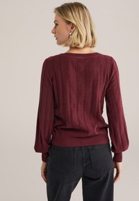 Burgundin neulottu neule, jossa on ribbikuvio, venepääntie ja pitkät hihat, yhdistettynä tummiin korkeavyötäröisiin farkkuihin.