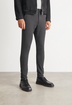 Pantaloni gri conici din material elastic, cu o textură netedă. Asortați cu pantofi negri cu șireturi și o jachetă din denim neagră.
