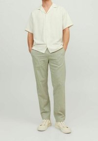 Kortärmad, knapp-up skjorta i off-white tyg; matchad med ljusgröna, texturerade byxor och krämfärgade sneakers.