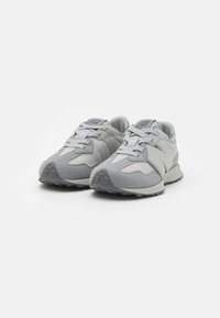 Jasnoszare sneakersy New Balance z detalami ze skóry zamszowej i siateczki, zawiązane, umieszczone obok siebie na białym tle.