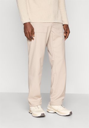 Pantaloni bej, cu croi lejer, dotati cu două buzunare frontale, asortați cu adidași de culoare deschisă. Textură moale, design casual.