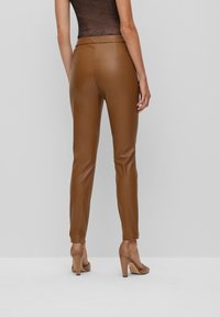 Bruna imitationläderbyxor med en slim fit, som har en mjuk textur och hög midja. Bärs tillsammans med beige högklackade skor.