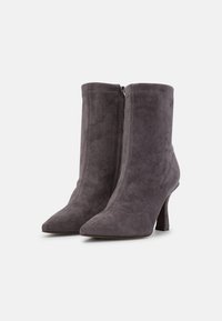 Szare zamszowe botki za kostkę z wąskim noskiem, średniej wysokości obcasem i bocznym suwakiem. Gładka faktura i dopasowany krój.