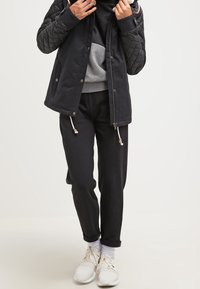 Veste matelassée noire avec un sweat à capuche gris, un pantalon de survêtement noir et des chaussures de sport blanches. Comprend des cordons de serrage et des textures contrastées.