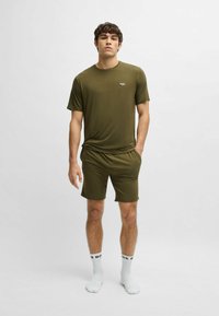 Olijfgroen activewear-set bestaat uit een aansluitend T-shirt met korte mouwen en shorts, gemaakt van een gladde, lichte stof, met een logo-detail.