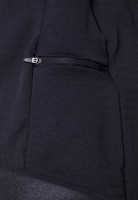 Svart sporttopp med en strukturerad tyg, dragkedjefickdetalj och en tapered design med en kontrasterande fåll.