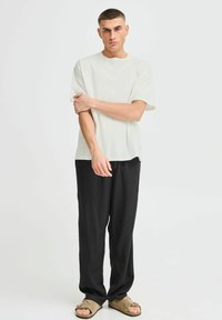 Light gray short-sleeve t-shirt paired with loose black pants. The outfit features a relaxed fit and is complemented by brown sandals.