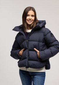 Granatowa kurtka puchowa z wysokim kołnierzem i kapturem, z grubym wypełnieniem, z przodem na zamek błyskawiczny i prążkowanym dołem. Widoczne są dwa boczne kieszenie na zamek.