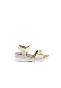 Sandalo beige con cinturino in velcro, materiale scamosciato morbido, cinturino alla caviglia regolabile, suola bianca con accento argentato e dettagli decorativi in oro.
