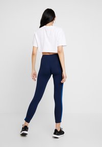 Marina leggings med blå sidosträck, stretchigt tyg och hög midja, tillsammans med en croppad vit t-shirt. Svarta träningsskor är på.