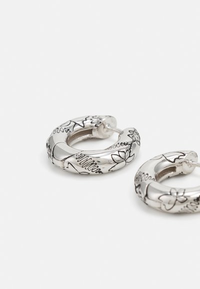 Les boucles d'oreilles en argent ont des motifs floraux gravés et une surface lisse et polie avec une forme légèrement courbée.