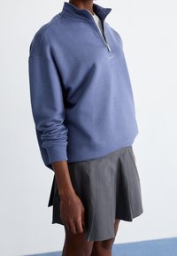 Ljusblå hoodie med dragkedja, långa ärmar och ribbad mudd, i kombination med en grå skorts med veck. Slät tygtextur, sportig design.