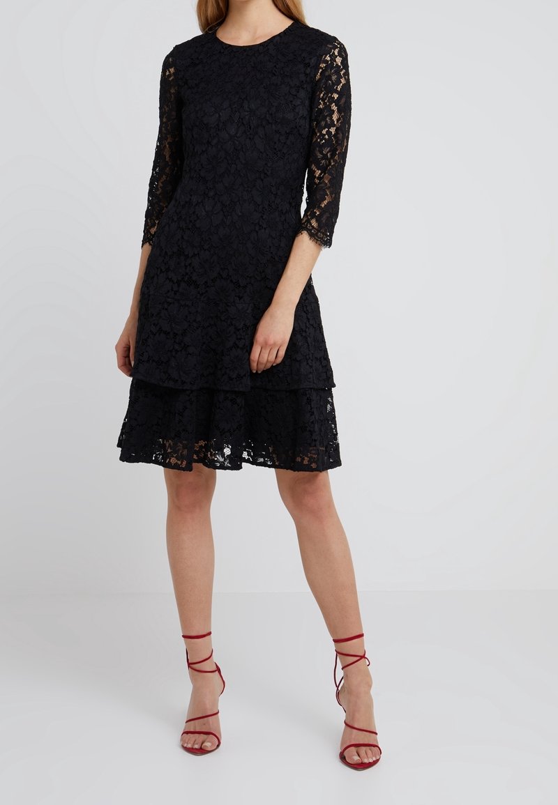 Robe en dentelle noire avec des manches 3/4, un ourlet à volants en tierces, un col rond et de délicats motifs floraux. Assortie à des talons rouges à lanières.