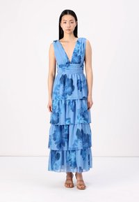 Zila, čīlota kleita ar dziļu V veida kakla izgriezumu, ziedu raksts ar dažādām zila toņiem, iešūta josta un plūstoša auduma. Brūni sandales piešķir izskatam pabeigtību.