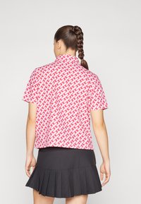 Short-sleeve shirt in a pink and white woven pattern, featuring a collar. Worn with a black pleated skirt, showing a relaxed fit.