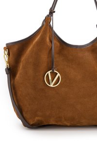 Bruine suède handtas met donkerbruin leren afwerking. Voorzien van een gouden cirkelvormige logocharme die is bevestigd met een leren strap. Soepele textuur.