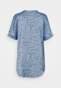 Top azzurro chiaro a maniche corte con un motivo a pois neri. Il tessuto appare liscio con una silhouette leggermente ampia e un collo arrotondato.
