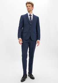Granatowy garnitur z fakturowanej tkaniny, slim fit, na dwa guziki, z wyłogami, połączony z białą koszulą i wąskim krawatem w paski, czarne buty.
