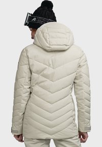 Beige gefütterte Jacke mit einem Zickzackmuster, ausgestattet mit einer großen Kapuze, elastischen Bündchen und einer glatten, glänzenden Oberfläche.